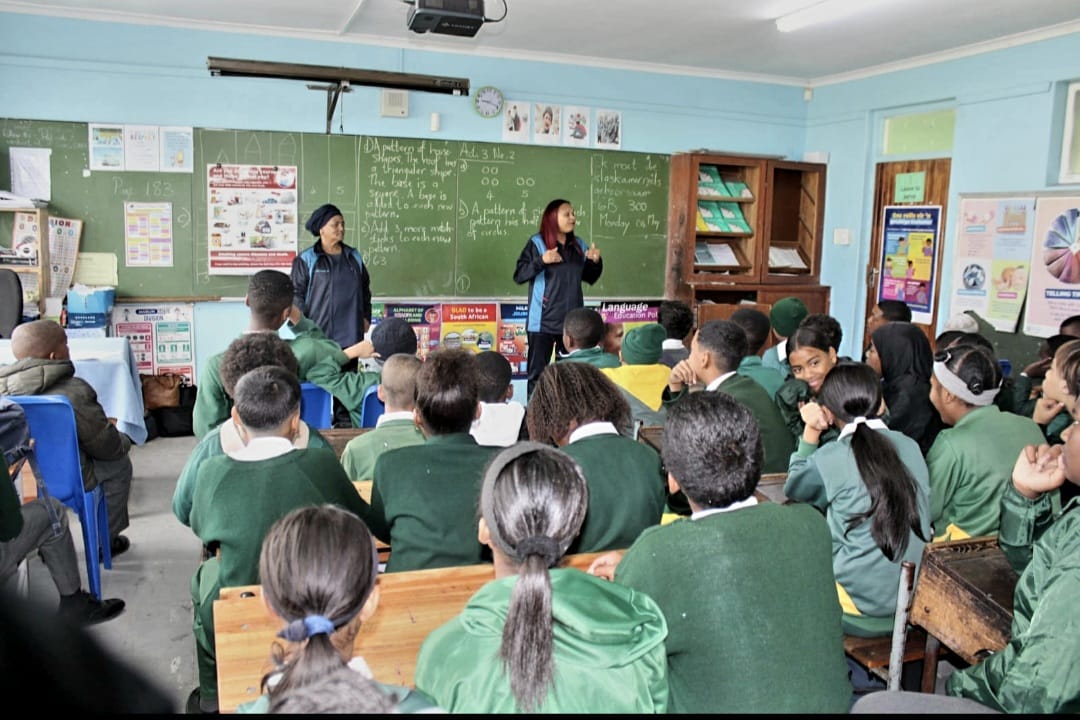 IPI team members presenting to a classroom of learners as part of a school feeding scheme and health outreach